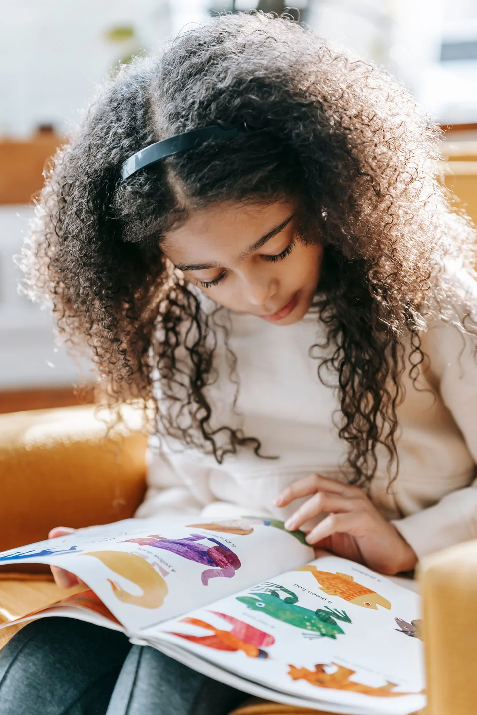 Anak duduk santai sambil membaca buku bergambar di rumah