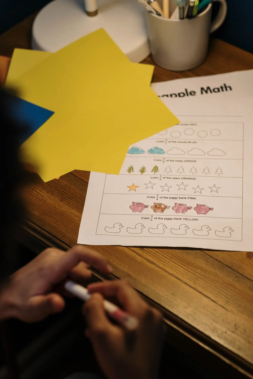 Anak mengerjakan worksheet berhitung sederhana di meja kayu